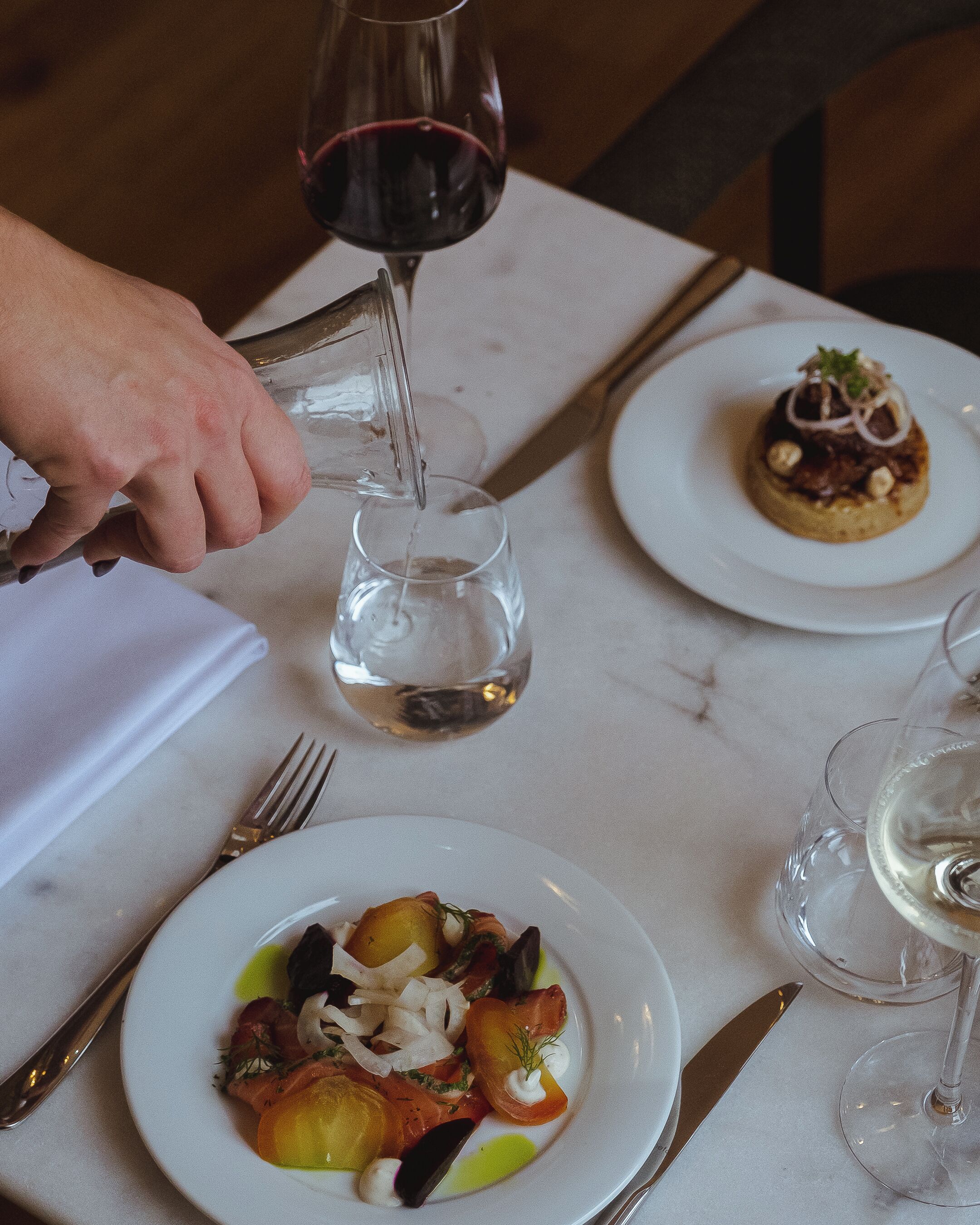 A dining table with plates of food, a glass of red wine, and a glass of white wine.