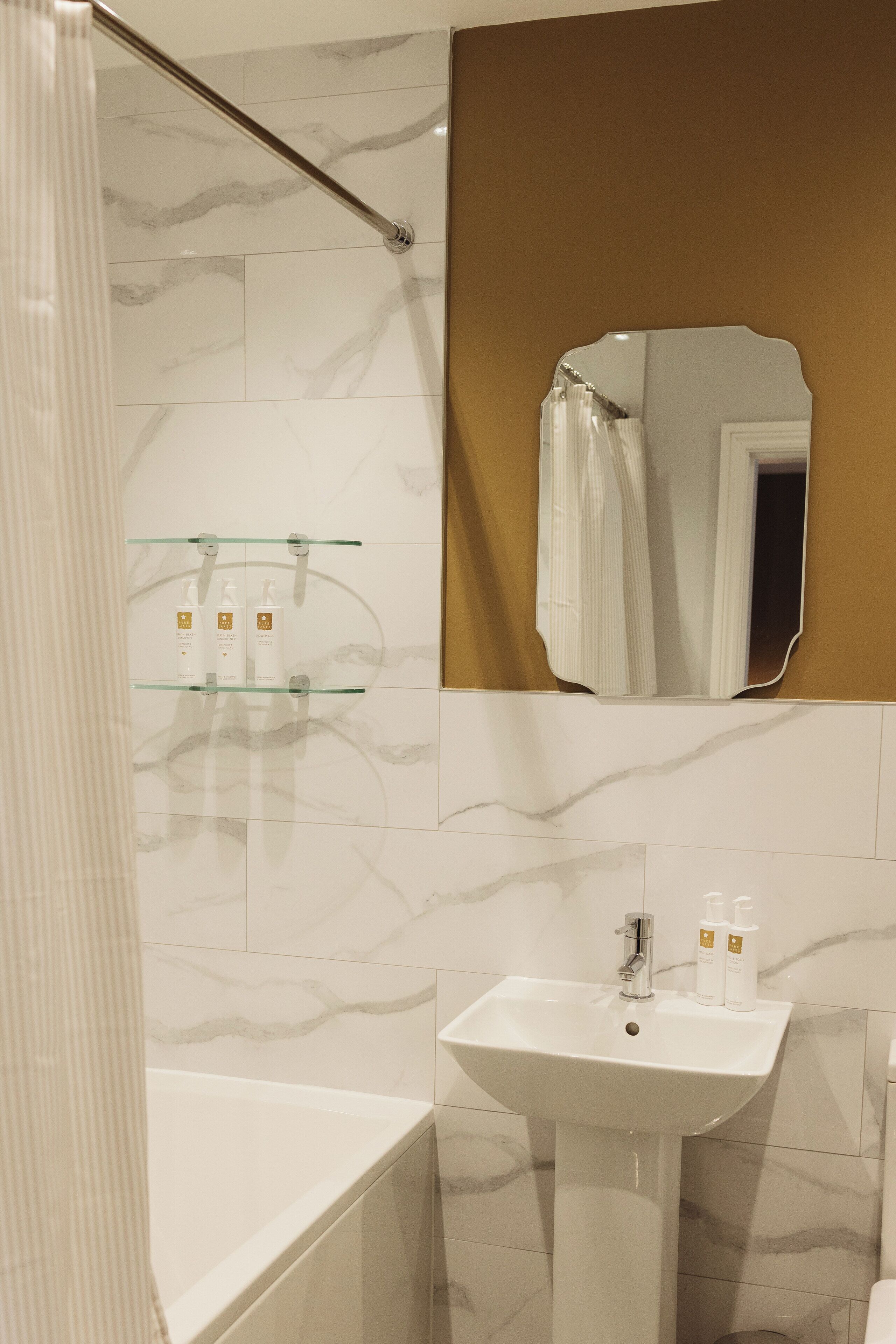 A bathroom with a bathtub, a sink, and a glass shelf with toiletries.