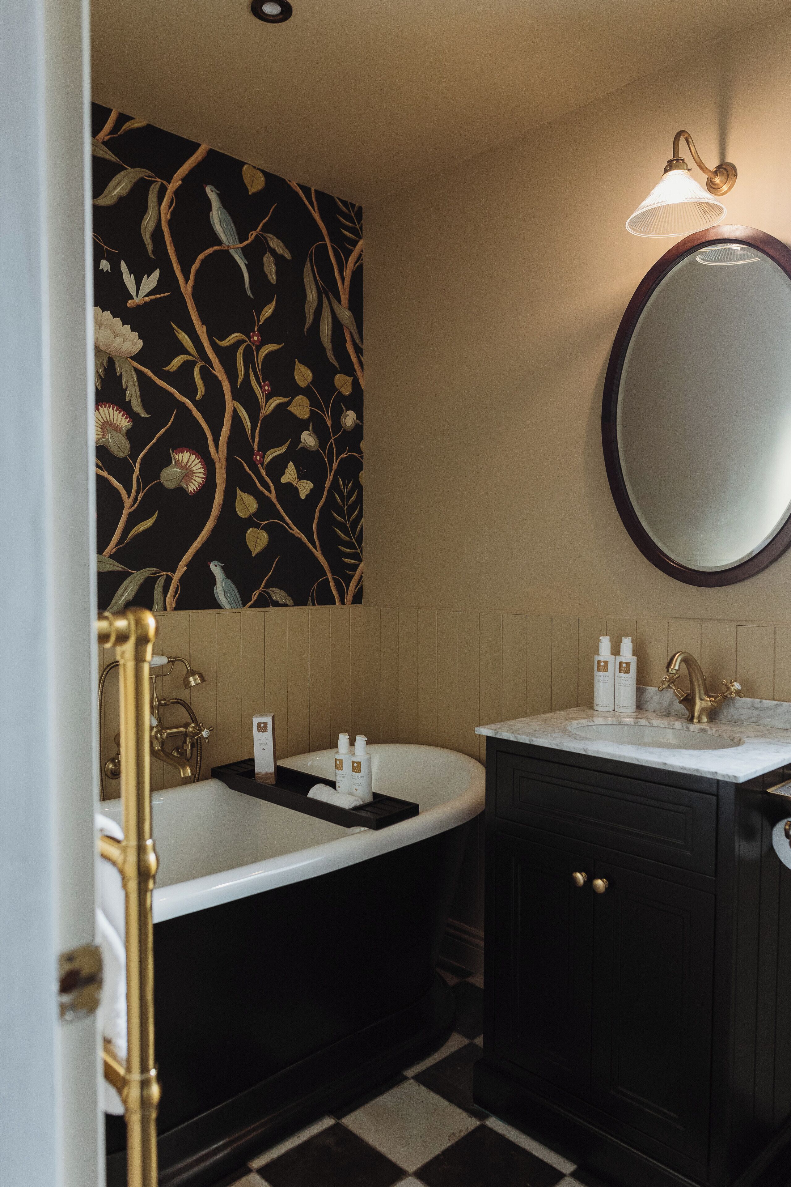 A bathroom with a black and white checkered floor, a black bathtub, a white sink with a gold faucet, and a mirror with a gold frame.