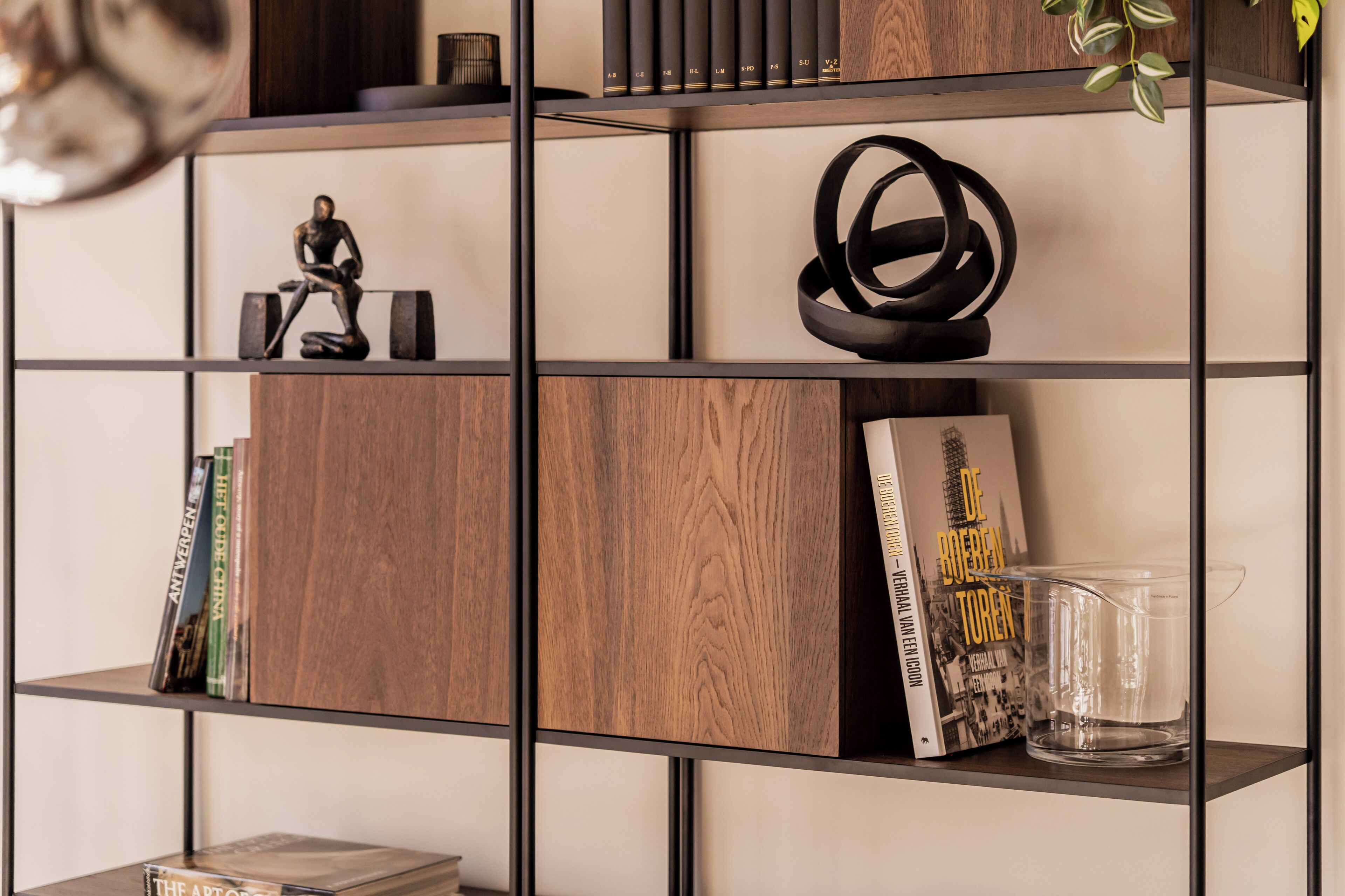 A bookshelf with books, a decorative figure, and a clear glass pitcher.