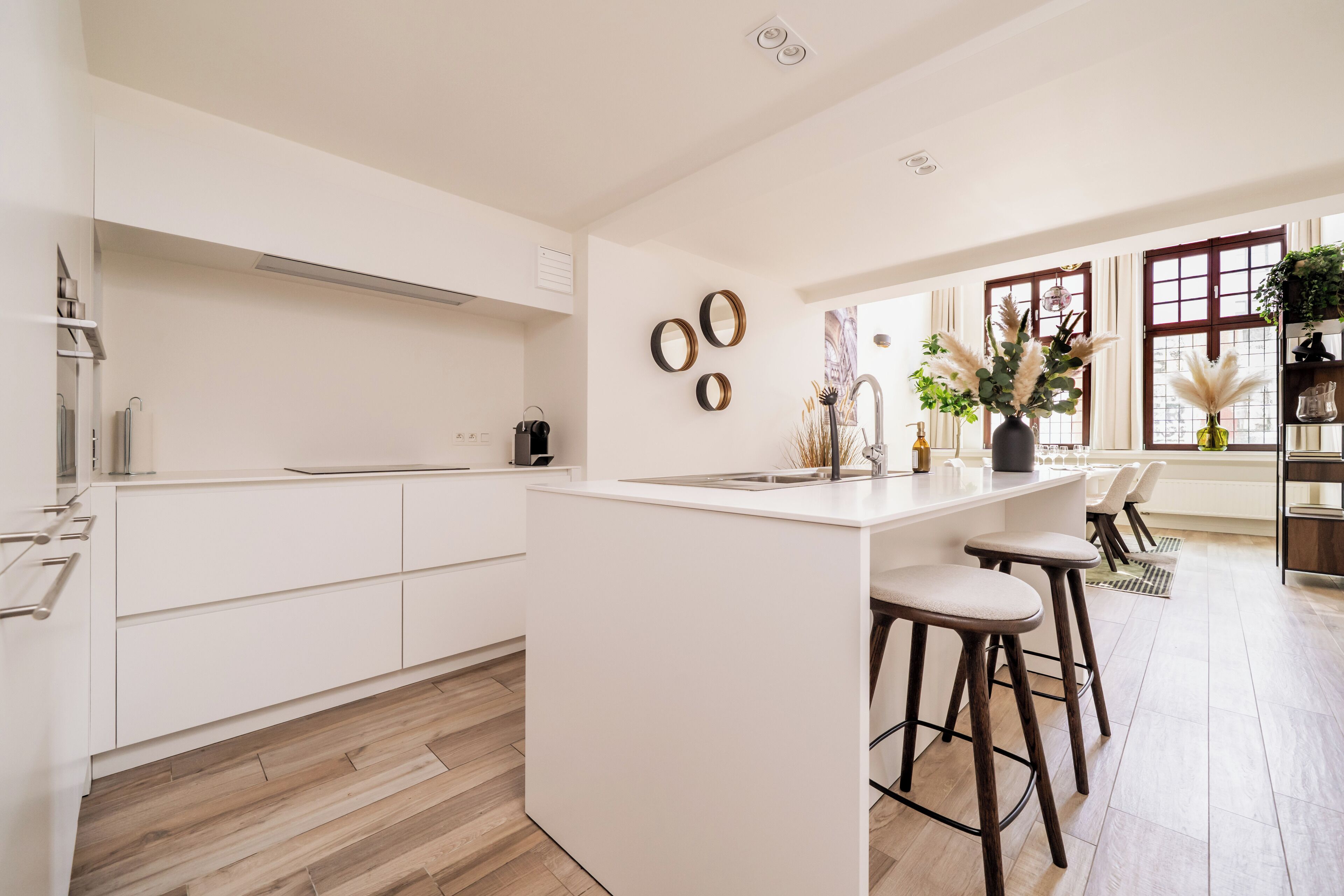 A modern kitchen with white cabinetry, a central island with stools, and decorative mirrors on the wall.