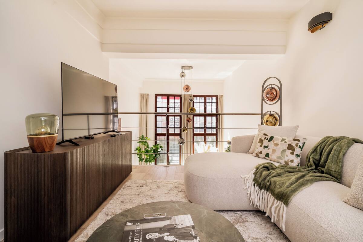 A modern living room with a sofa, a TV, and a wooden console. There is a staircase leading to another room.