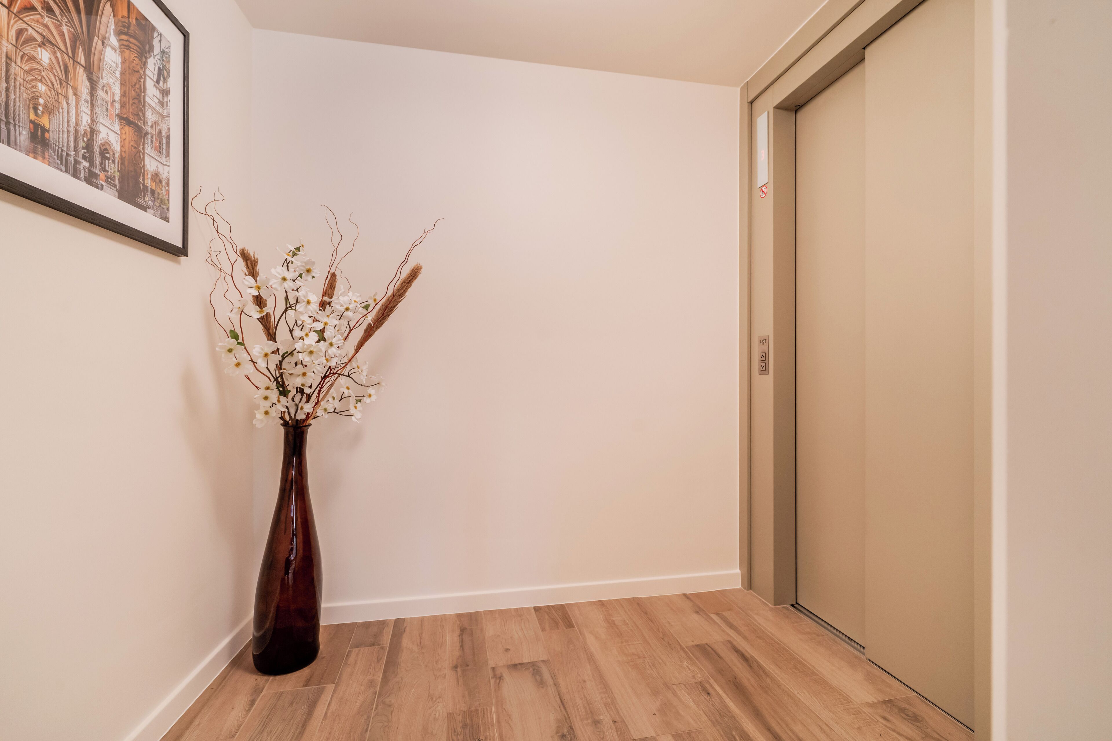 A hallway with a wooden floor, a vase with dried flowers, and a door.