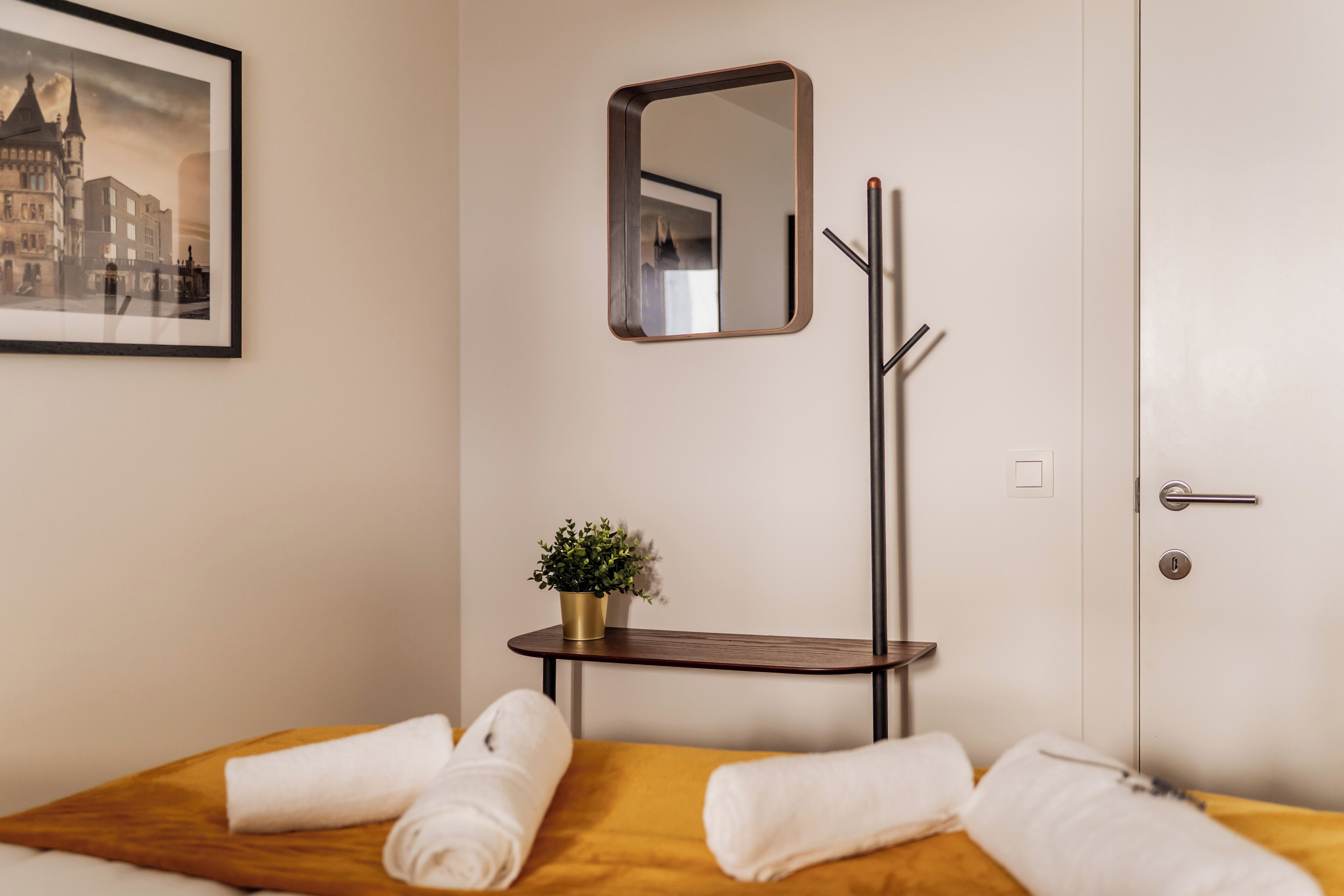A hotel room with a bed, towels, a small table with a plant, a mirror, and a door.