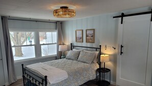 Un dormitorio con una cama, dos lámparas de noche, una ventana con cortinas y una puerta.