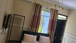 A hotel room with a bed, curtains, a wardrobe, and a window with a view. - Maggie Resthouse (Dar es Salaam)