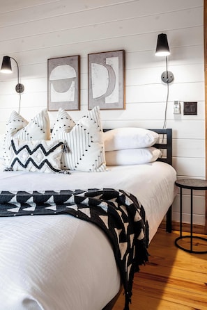 A neatly made bed with patterned pillows, a black throw blanket, and two wall-mounted lamps.