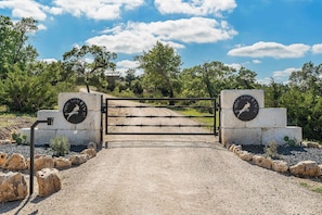 A gated entrance with a gravel path leading through it, surrounded by rocks and greenery.