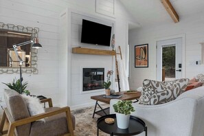Un salon doté d’une cheminée, d’un téléviseur fixé au mur, d’une table basse en bois et d’un canapé agrémenté de coussins à motifs.