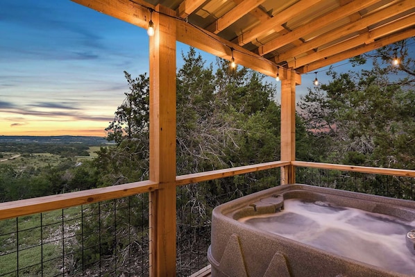 A hot tub under a wooden pergola with a view of a forested landscape.