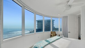 Une chambre avec un grand lit, une chaise et une vue sur l’océan et les bâtiments.
