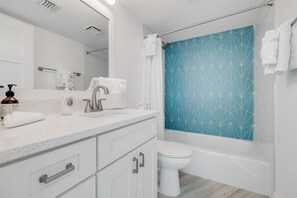 Features a sleek vanity with sink and large mirror, a toilet, and a shower with a geometric-patterned door.