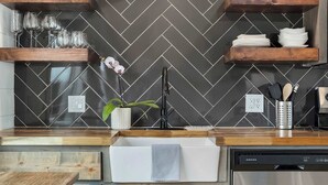 A kitchen with wooden shelves, a dishwasher, and a herringbone tile backsplash.