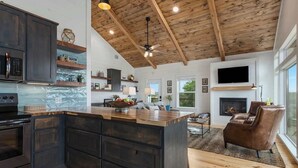 A modern kitchen with dark cabinetry, a central island, and a wooden ceiling. - Modern Ranch Retreat with Hill Country Views (Gillespie County)
