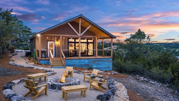 A wooden cabin with a covered porch, outdoor seating, and a fire pit. - Modern Ranch Retreat with Hill Country Views (Gillespie County)