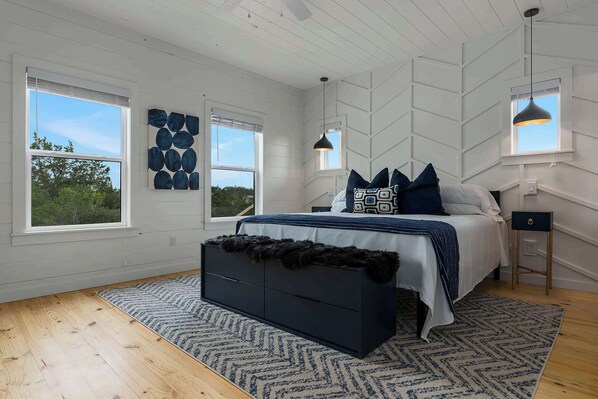 Une chambre à coucher avec un lit, une commode, deux fenêtres et un ventilateur de plafond.