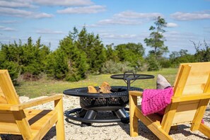 Un pozo de fuego con leña, una mesa redonda y dos sillas de madera en un entorno natural.