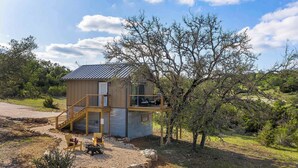 A small cabin with a wooden staircase, a deck, and a fire pit in the yard. - Treehouse Retreat with Hill Country Views (Gillespie County)