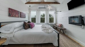 A bedroom with a bed, a TV, a fireplace, and artwork on the wall. - Treehouse Retreat with Hill Country Views (Gillespie County)