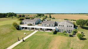 A large, modern building with a covered patio area, surrounded by expansive grassy fields and a clear sky. - Les Villas du Parc de la Chabotterie (Montréverd)