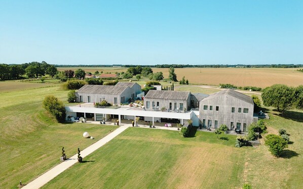 A large, modern building with a covered patio area, surrounded by expansive grassy fields and a clear sky.