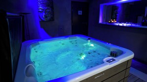 A hot tub with a control panel, surrounded by a bathroom with a mirror and a Buddha statue. - Les Villas du Parc de la Chabotterie (Montréverd)