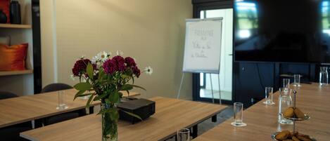 Un salón de conferencias con una larga mesa, un proyector, una pizarra y un jarrón con flores.