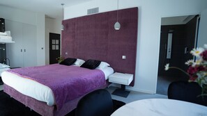 A modern hotel room with a large bed, a bedside table, a desk, and a shower area.