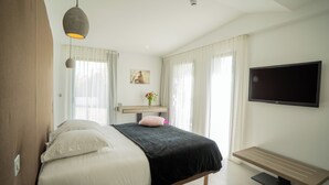 A modern bedroom with a bed, a desk, a TV, and a window with curtains. - Les Villas du Parc de la Chabotterie (Montréverd)