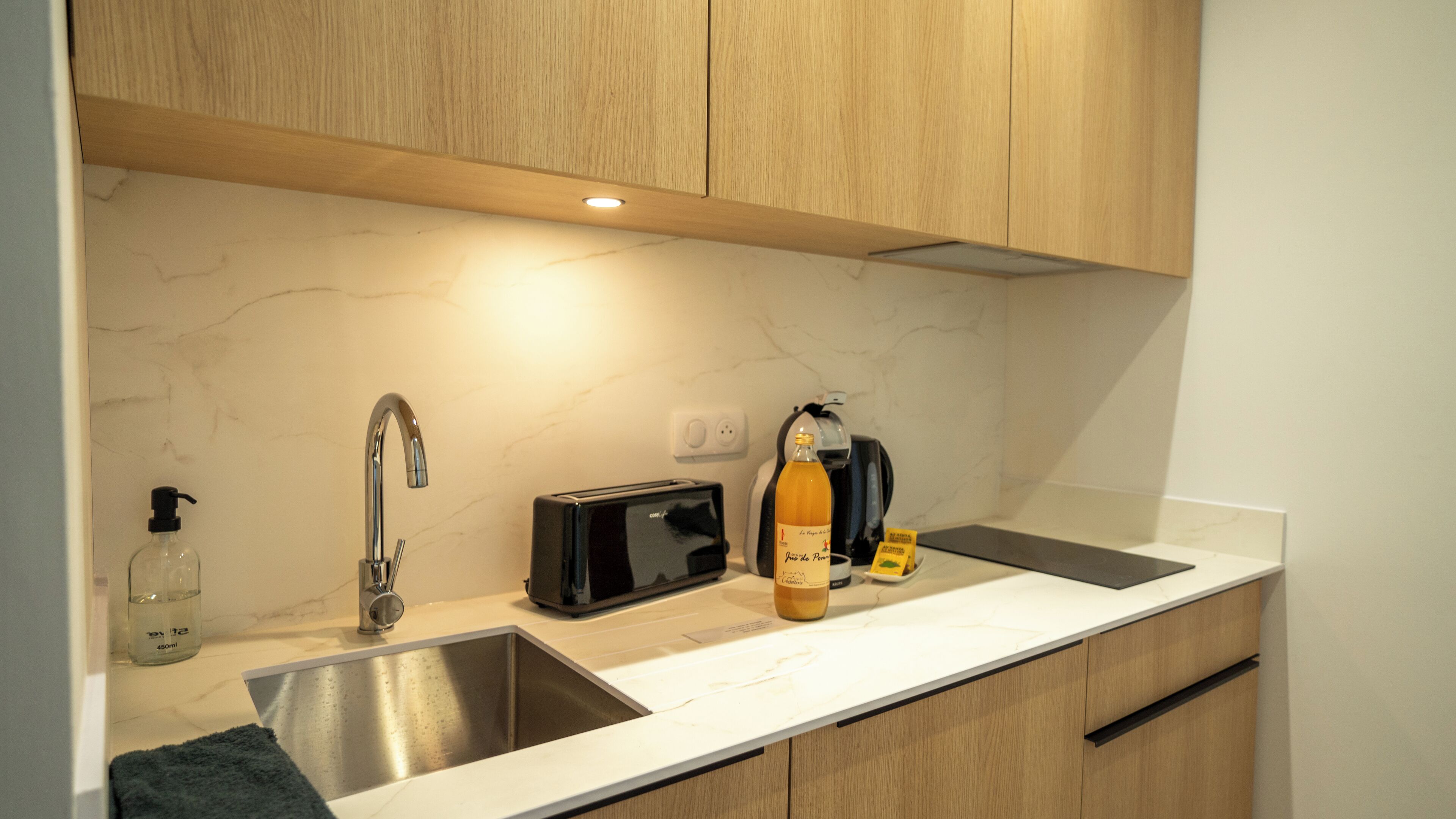 A modern kitchen with wooden cabinets, a stainless steel sink, a black toaster, a bottle of orange juice, and a coffee maker.