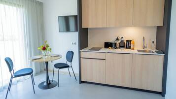 A modern kitchen with a dining area, including a table with chairs, a TV mounted on the wall, and various kitchen appliances.