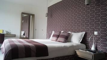 A neatly made bed with a patterned headboard, a bedside table with a lamp, and a mirror on the wall.
