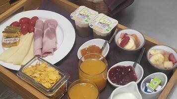 Bandeja de desayuno con croissants, jamón, queso, yogur, fruta y bebidas.