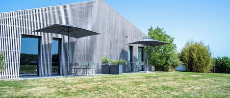 A modern building with a vertical wooden facade, large glass windows, and outdoor seating with umbrellas.
