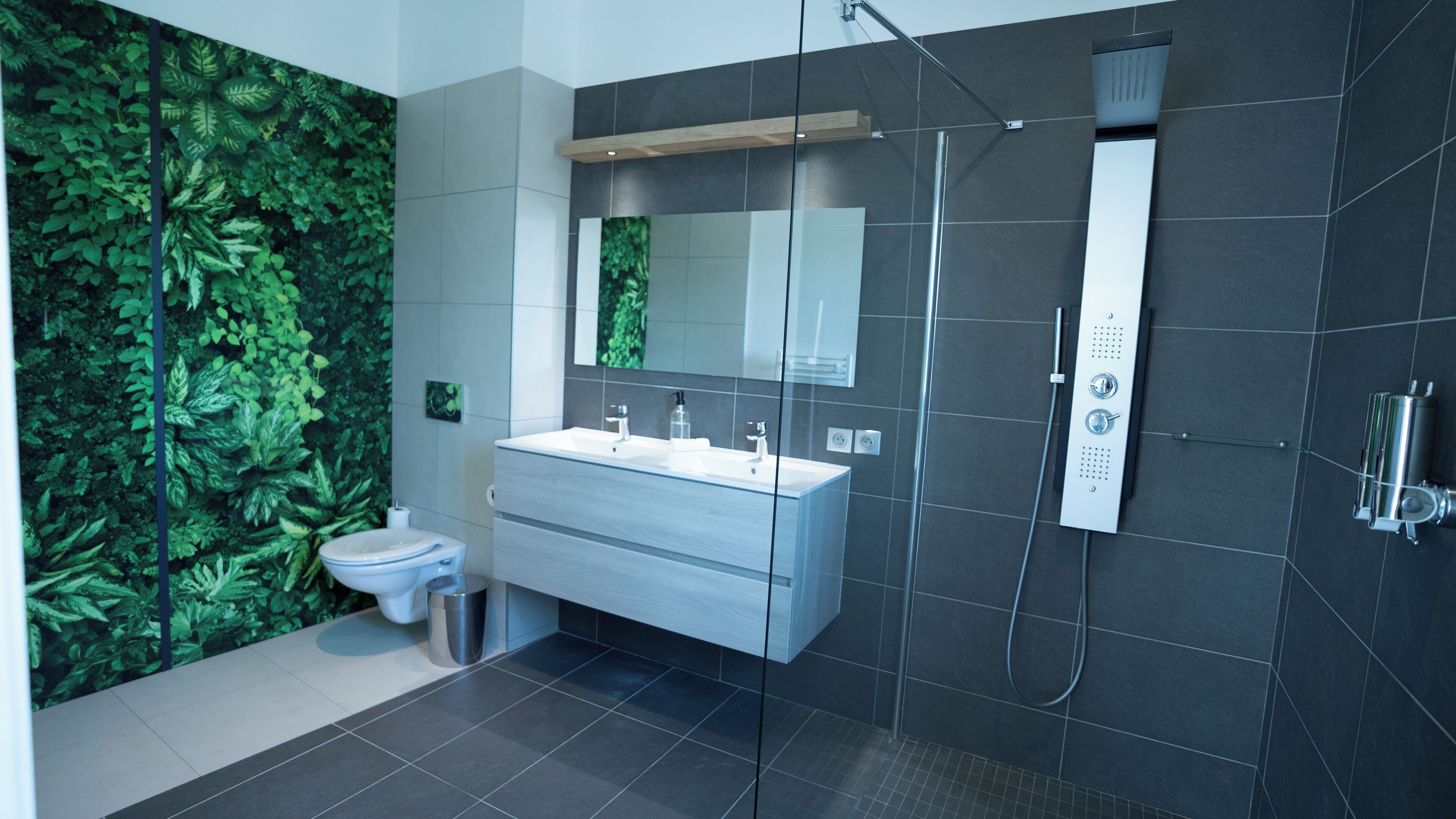 Un baño moderno con una pared cubierta de follaje verde, un lavabo blanco y una cabina de ducha de vidrio.