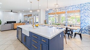 Una cocina moderna con una isla grande, armarios azules e iluminación colgante.