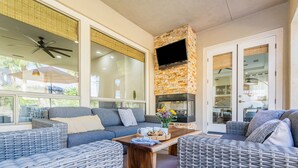 Una sala de estar moderna con muebles de mimbre, chimenea de piedra y ventanas amplias.