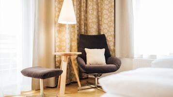 Ein modernes Hotelzimmer mit Holzboden, einem schwarzen Sessel mit Kissen, einem kleinen Holztisch und einer Stehlampe.