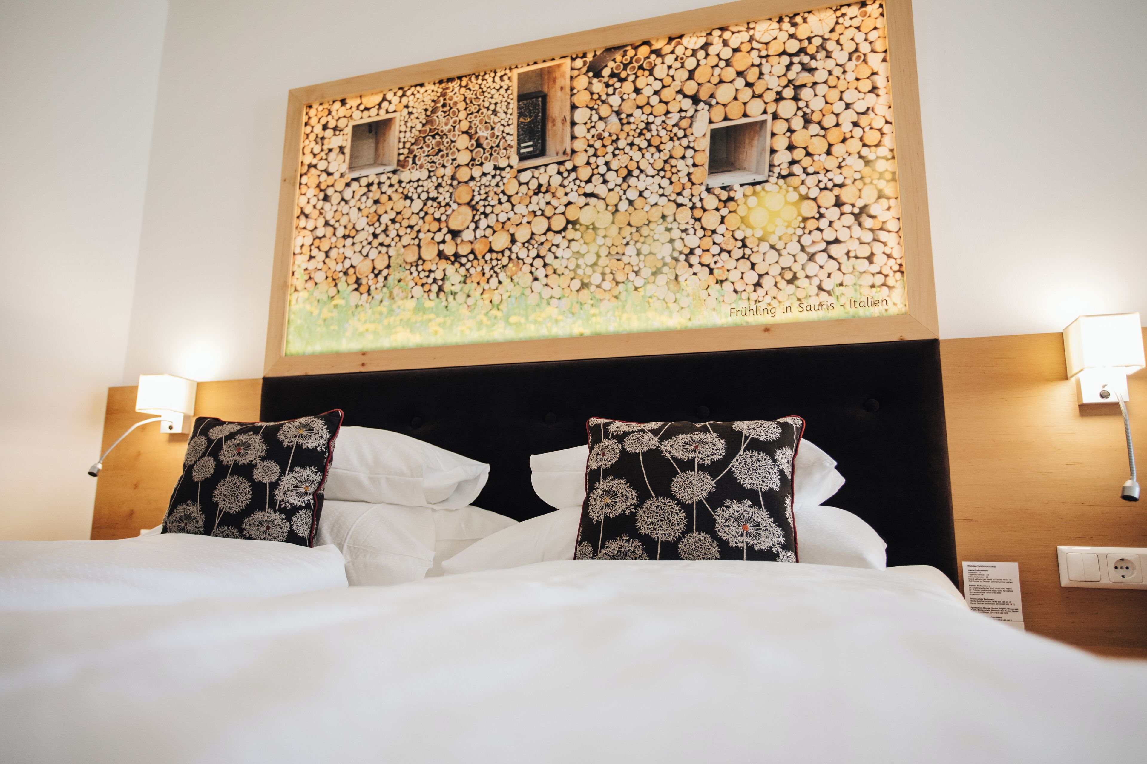 Ein Hotelzimmer mit einem Bett, weißer Bettwäsche, zwei Zierkissen, einem Kopfteil mit einer Wand aus Holzbalken und zwei Wandleuchten.