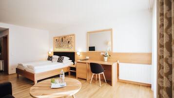 A hotel room with a bed, desk, chair, and a small table with a bottle and glasses.