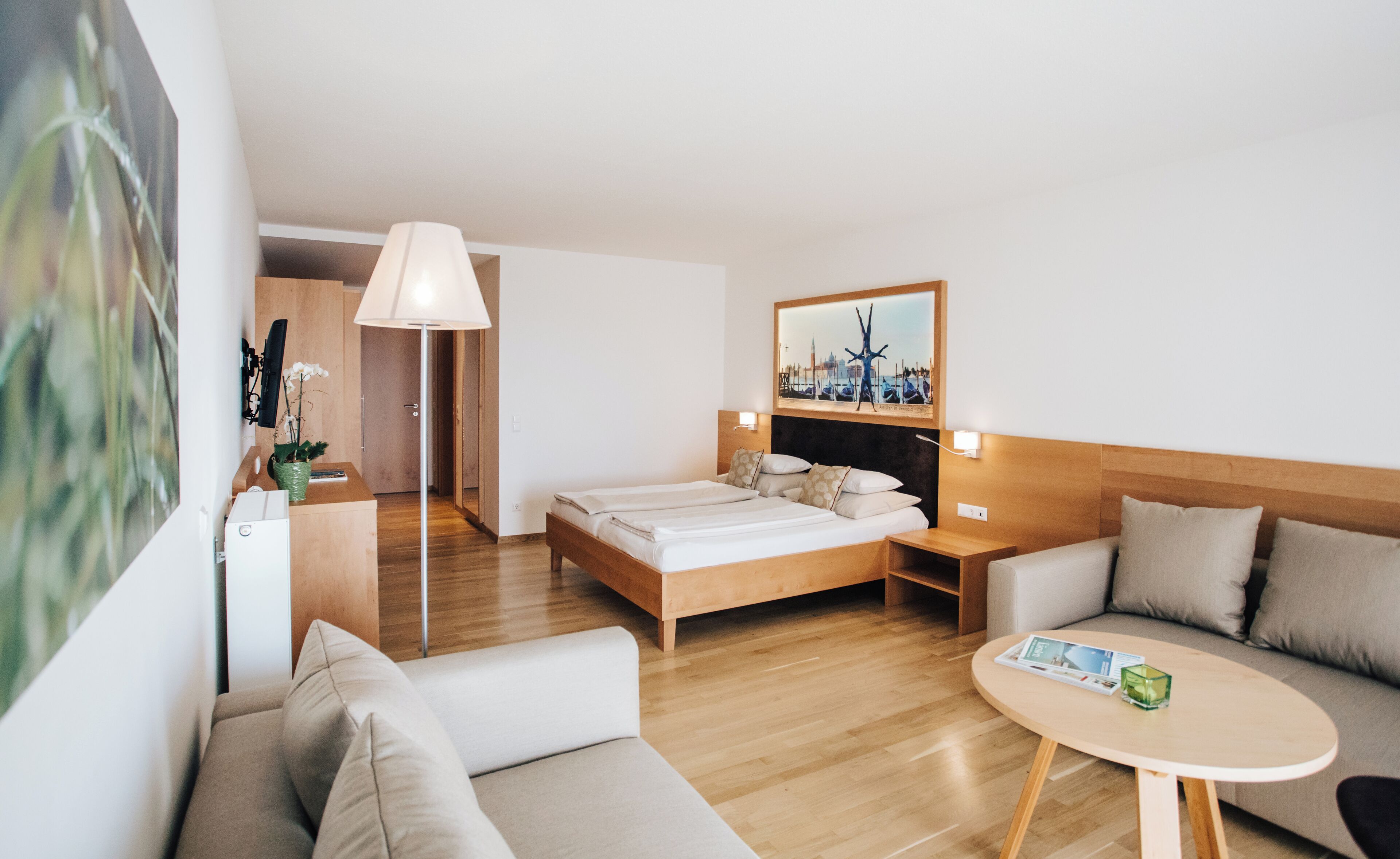 A modern hotel room with a bed, a sofa, a small table, and a mirror.