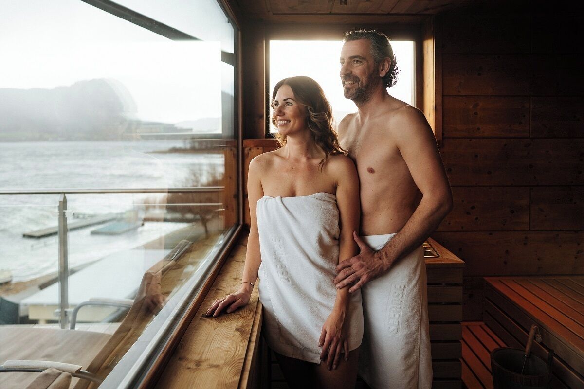A couple standing in a wooden cabin with a view of a body of water.