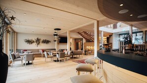 A spacious lobby with a wooden floor, seating areas, a bar, and a staircase.