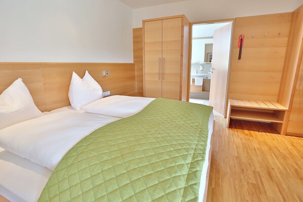 Une chambre d’hôtel avec un lit, une couvre-lit matelassée verte, une armoire en bois et une salle de bain visible à travers une porte ouverte.