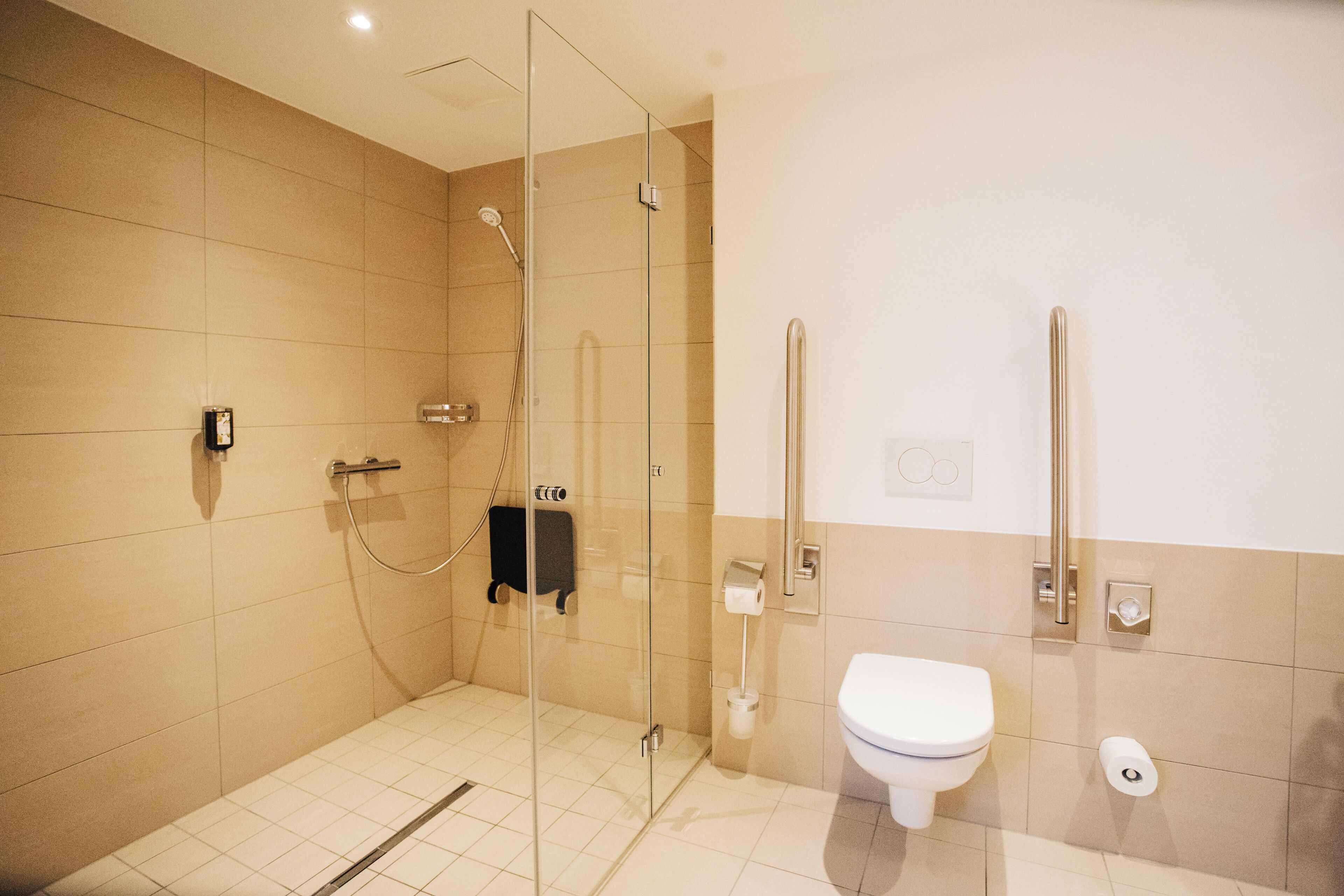 Un baño moderno con ducha de vidrio, inodoro blanco y barra de apoyo para accesibilidad.