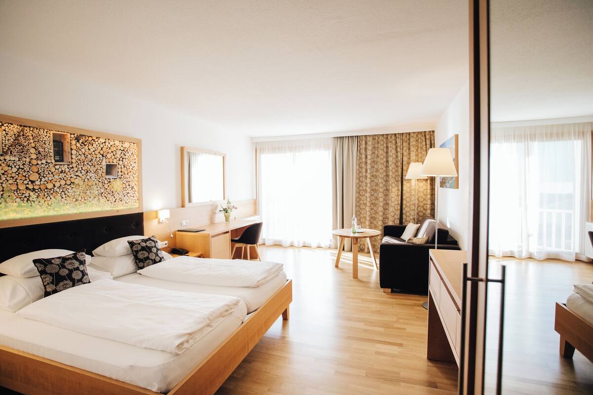 Ein Hotelzimmer mit zwei Betten, einem Schreibtisch, einem Sessel und einem großen Fenster mit Vorhängen.