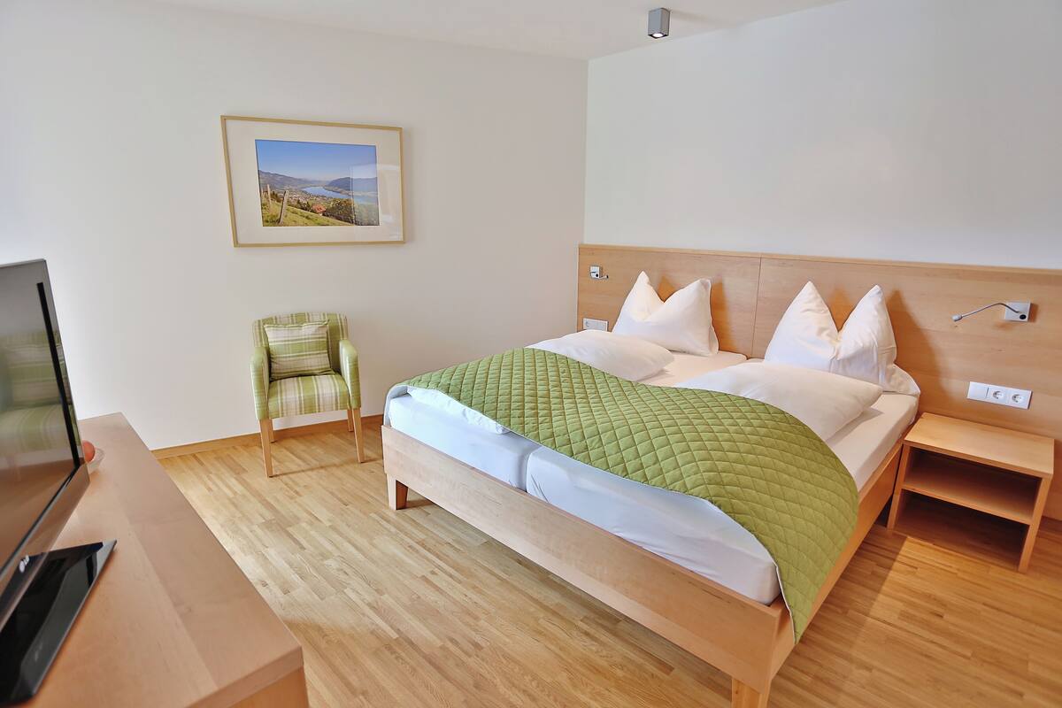 Ein Hotelzimmer mit einem Bett, einem Sessel, einem Fernseher und einem Gemälde an der Wand.