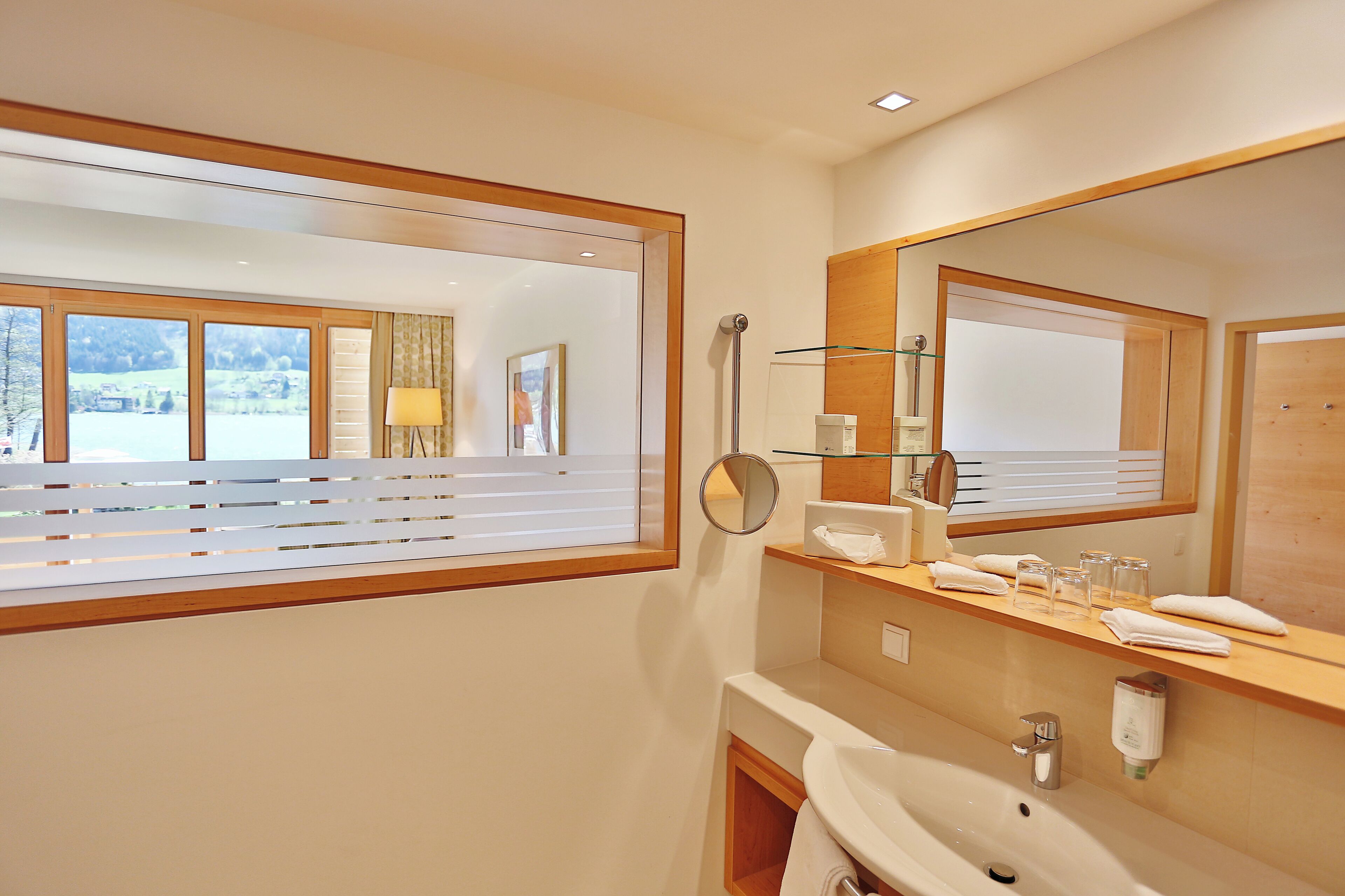 A modern bathroom with a large mirror, a sink, and a window with blinds.