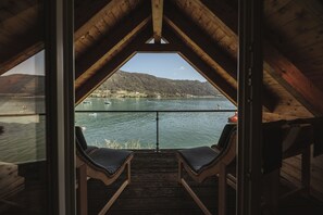 Une terrasse en bois avec deux chaises longues donnant sur un lac où l’on aperçoit des bateaux, et un paysage vallonné en arrière-plan.