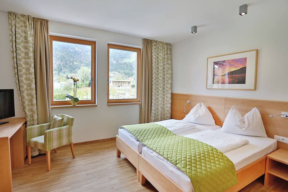Ein Hotelzimmer mit Bett, Schreibtisch, Stuhl und zwei Fenstern mit Blick auf die Berge.